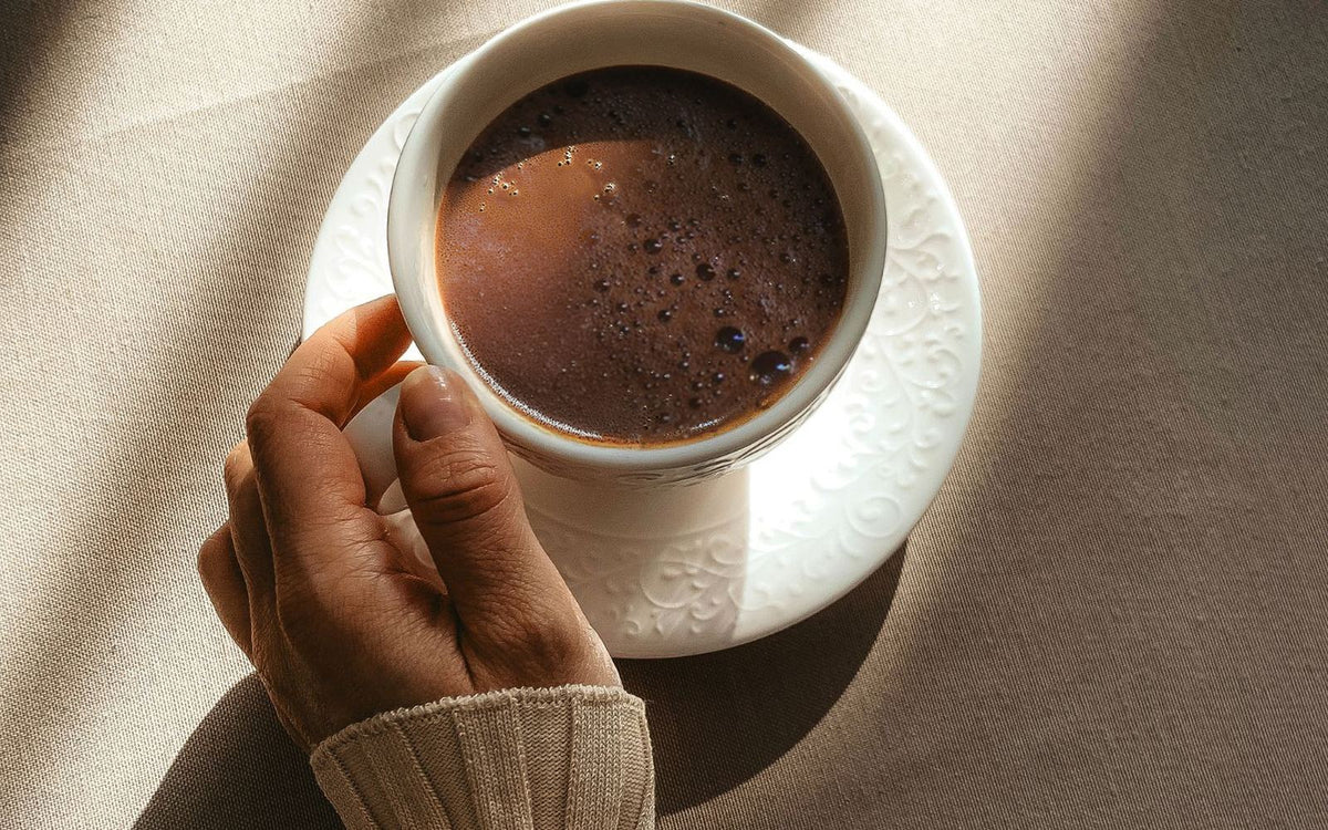 Tasse zeremonieller Kakao im Morgenlicht, eine Hand hält die Tasse auf der Untertasse