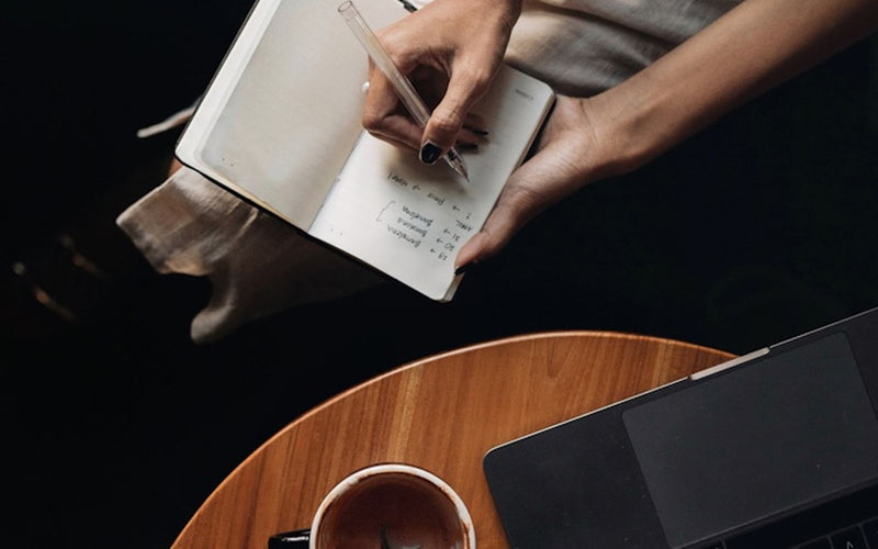Notizbuch, Tasse Kakao und Laptop auf einem Holztisch